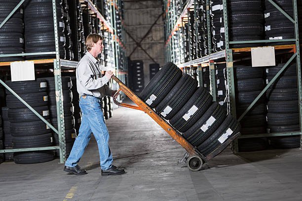 Mature man (40s) working in warehouse, moving stack of tires.