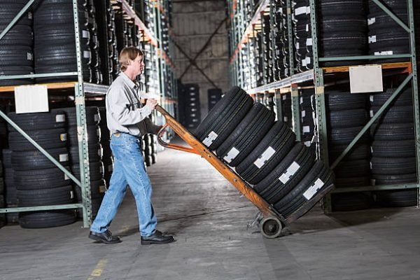 Mature man (40s) working in warehouse, moving stack of tires.